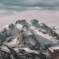 Snow-covered mountain range under cloudy sky Snowy mountain peaks with cloudy sky